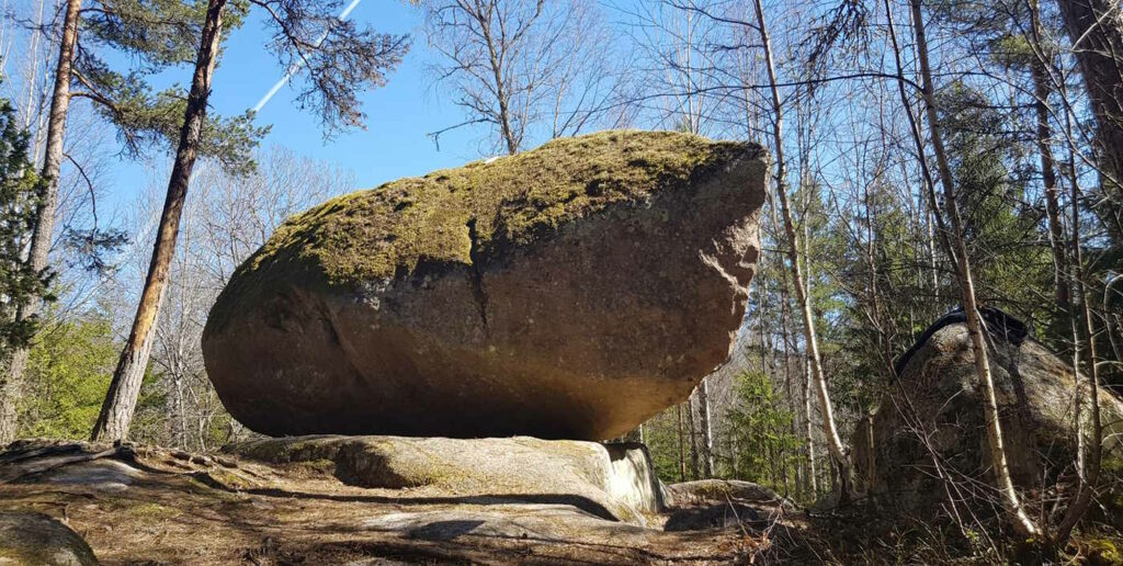 Ein riesiger, mit Moos bewachsener Felsbrocken liegt auf einem Felsplateau im Wald.